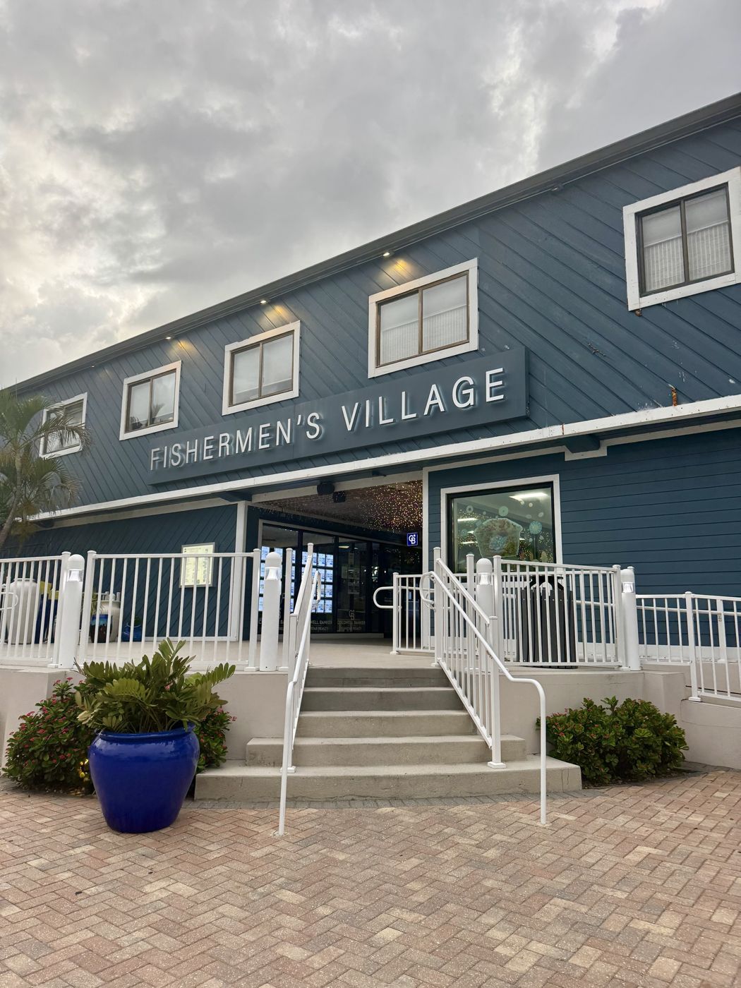 Blue waterfront building with a lit sign, white railings and a blue planter